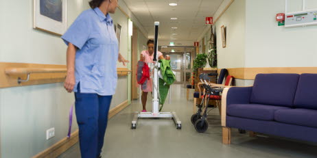Kvinnor i vårdkläder går i en korridor med arbetsutrustning som används inom vården.